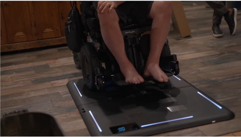A wheelchair user on Fold with one side of the chair on each panel, the edge lighting on and the display showing a reading.